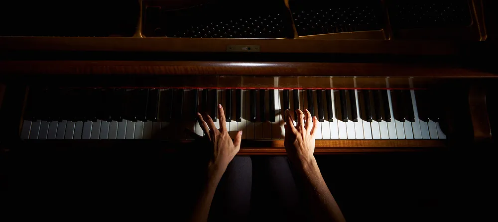 Hands playing a warmly lit piano, viewed from above